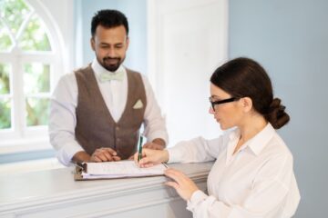 Businesswoman And Receptionist Filling Form Signing Papers Checking At Hotel